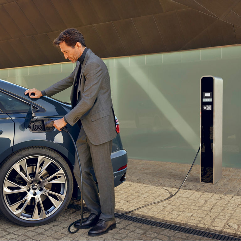 Person in a suit charging an electric car at a charging station.