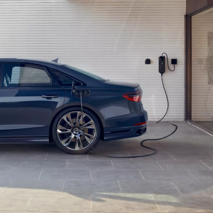 Blue electric car charging at a wall-mounted charging station.