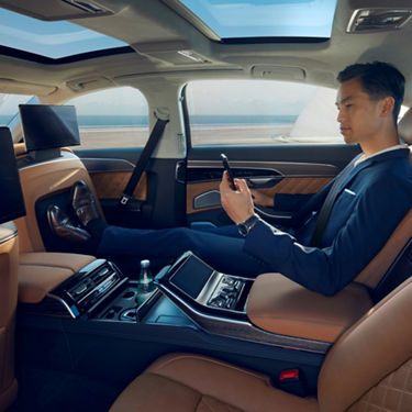 A person in a blue suit sitting in a luxury car interior, looking at a smartphone.