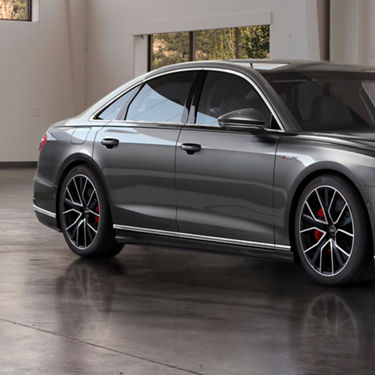 A grey sedan parked indoors, showcasing its profile and sporty wheels.