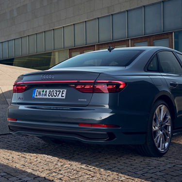Rear view of a parked Audi sedan with LED taillights on, in daylight.