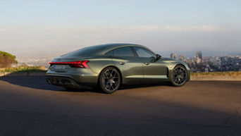 A green Audi RS e-tron GT performance parked on a hilltop overlooking a city skyline in the early evening