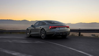 An Audi RS e-tron GT car driving on a highway in the early evening with a clear sky and mountains in the background