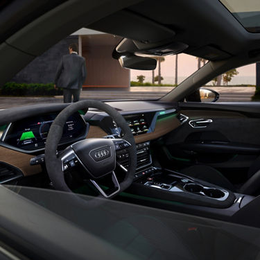 Interior view of an Audi car with steering wheel and dashboard, overlooking a man walking outside.