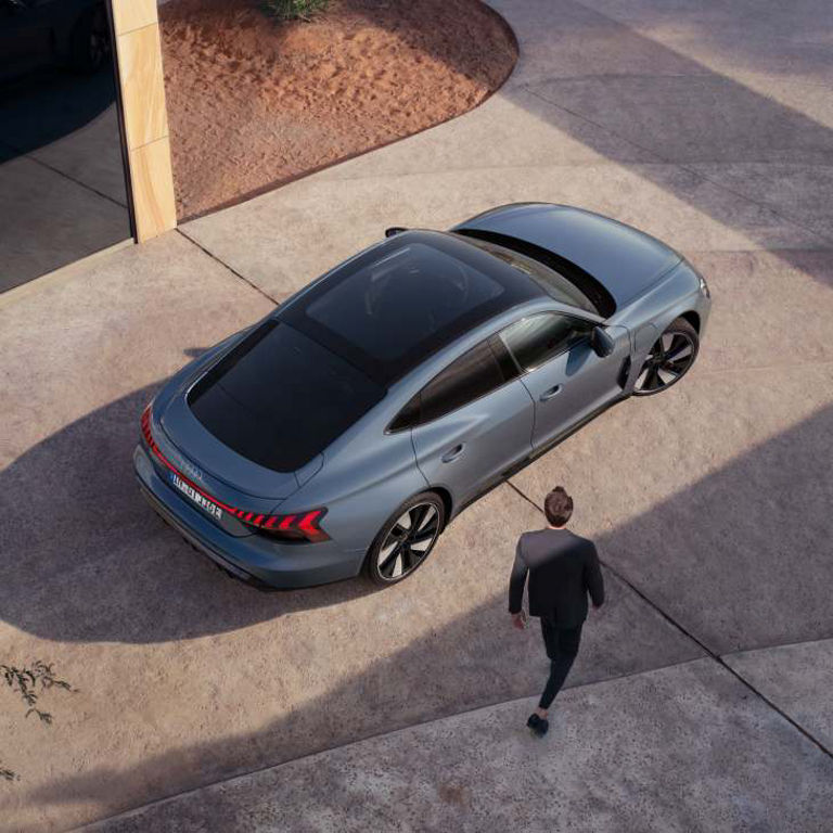 Aerial view of a grey sedan and a man walking towards it in a modern driveway setting.