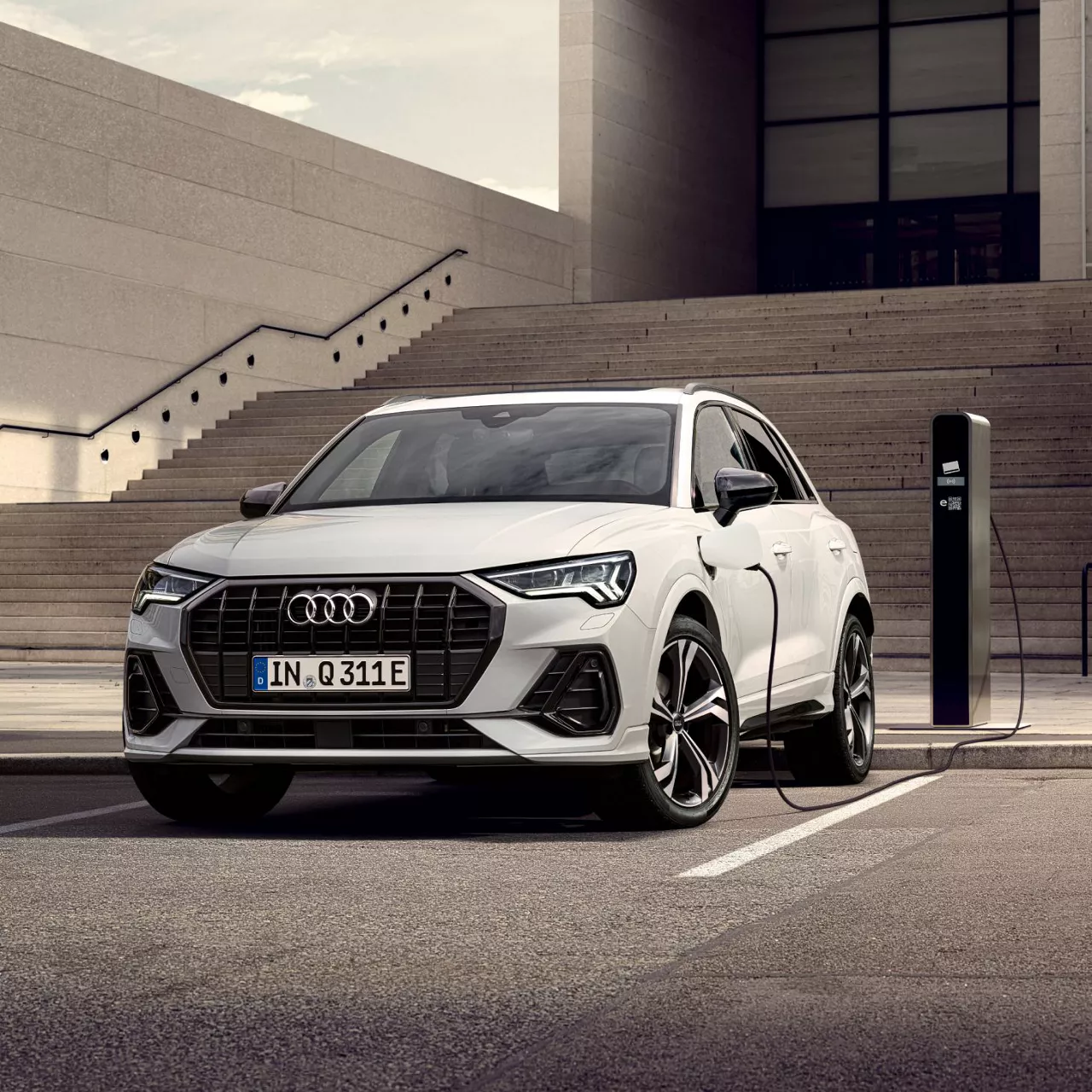 A white Audi electric vehicle on charge at a charge station in an urban setting