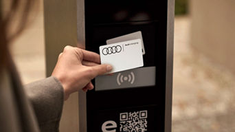 A woman holding up an Audi Charging card to a charge station terminal