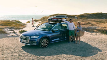 Mother & father beside a parked Audi vehicle, child in the distance walking towards the nearby beach