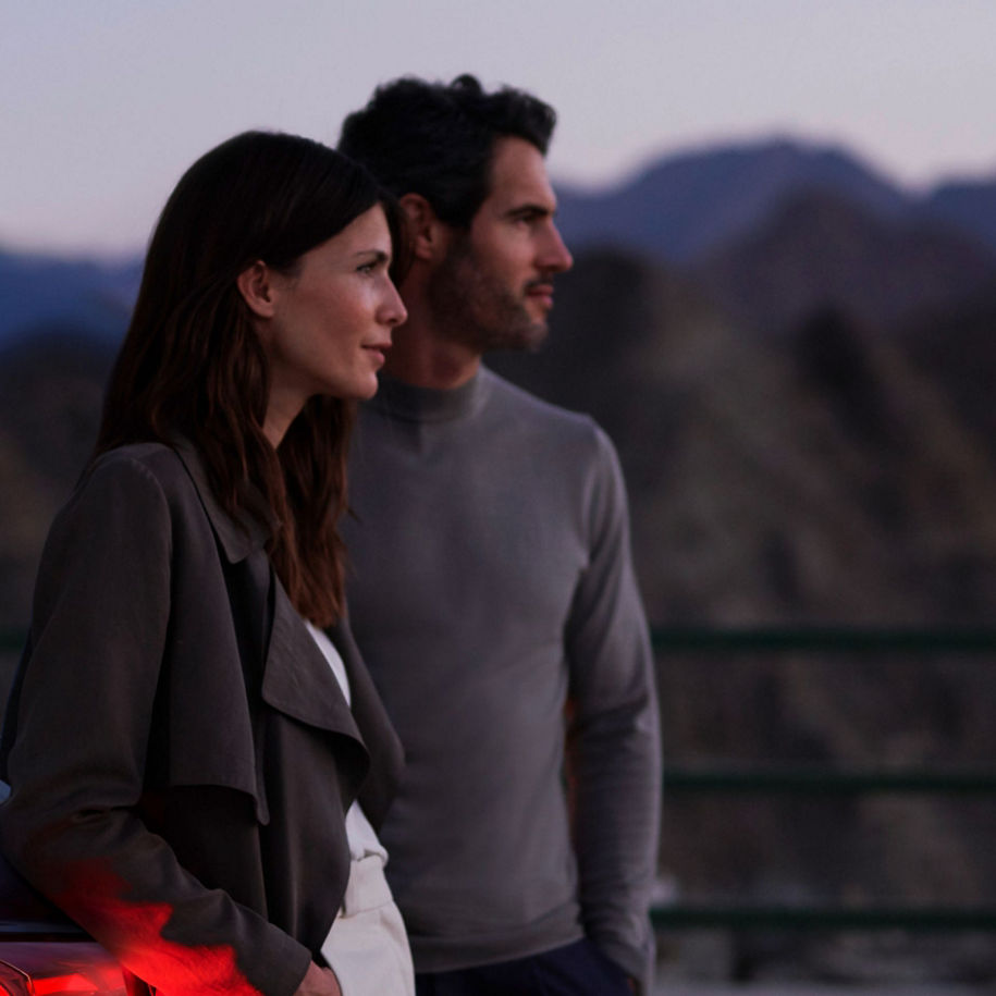 A couple standing close together with a mountainous backdrop at twilight.