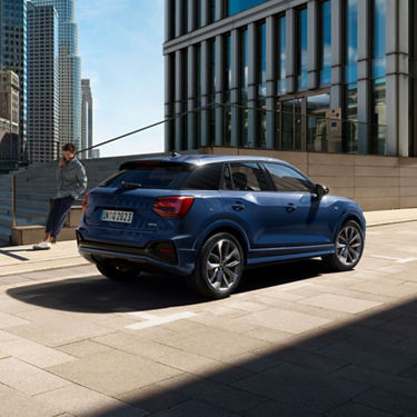 A blue SUV parked on a sunny city street with skyscrapers in the background.