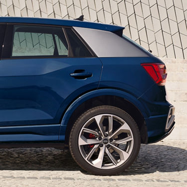 Blue SUV rear side view with intricate wheel design, parked by a unique tiled wall.