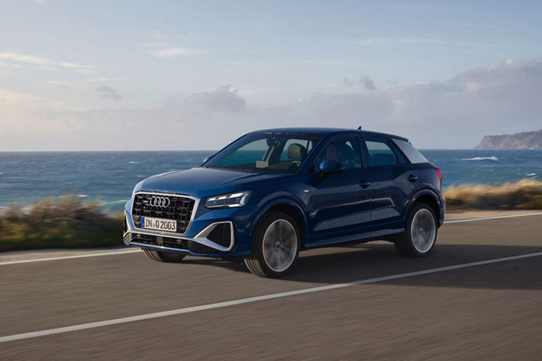 Blue Audi SUV driving along coastal road with sea and cliffs in the background.