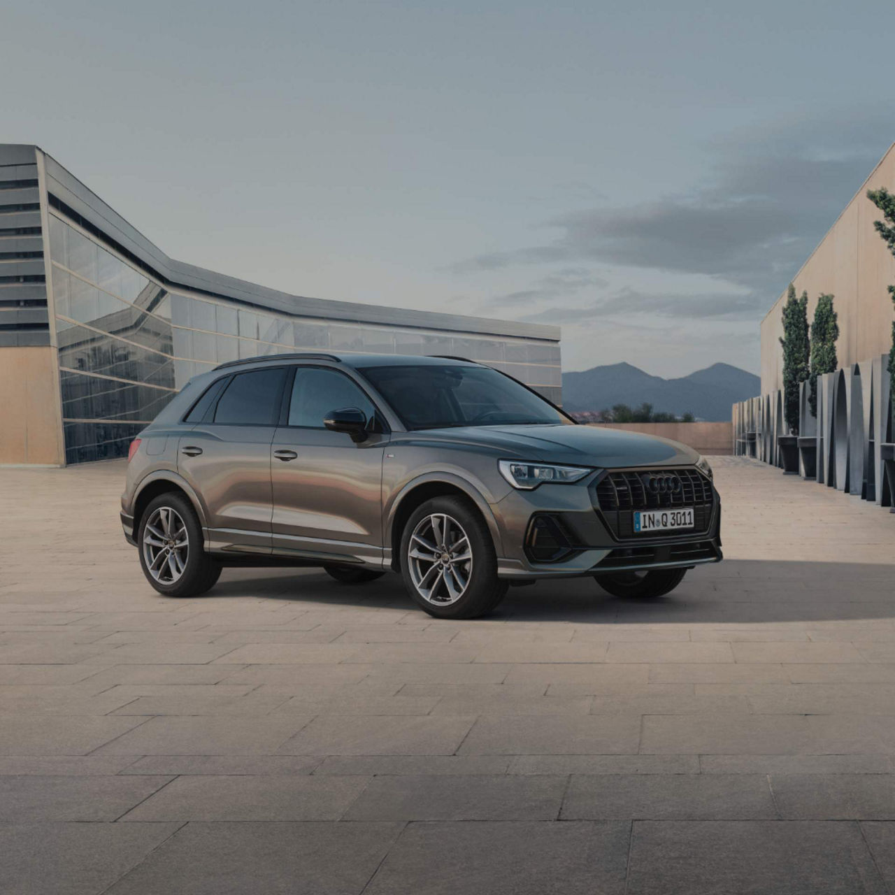 Audi Q3 parked in an open space in frony of modern building.