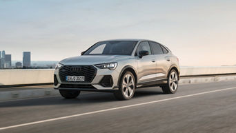 Silver Audi Q3 driving along a bridge with water and office buildings in the background