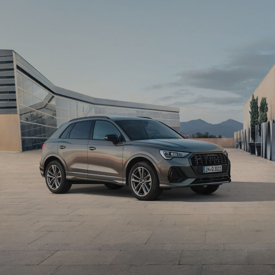 Lady in pink outfit approaching carbon coloured  Audi  Q3 outside building.