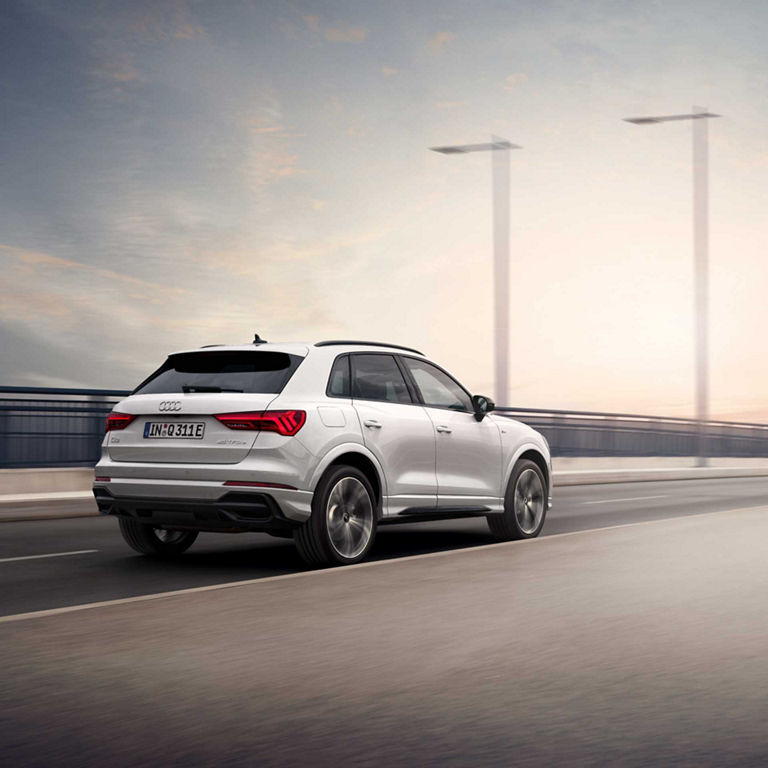 Rear perspective view of Audi Q3 TFSI e in motion moving away on the road.