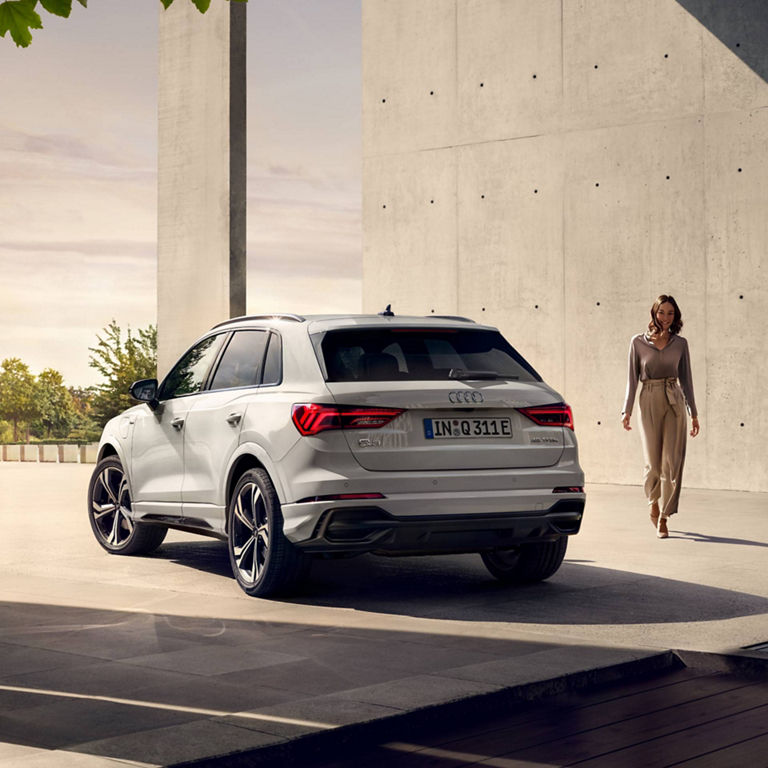 Rear perspective view of Audi Q3 TFSI e parked next to Lady.