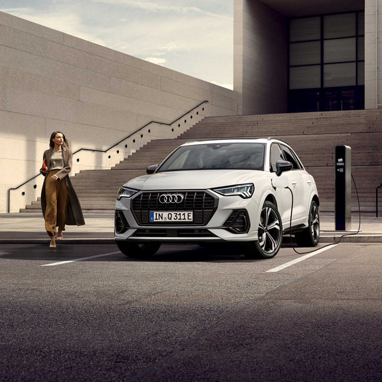 Lady stepping off kerb next to charging  white Audi Q3.