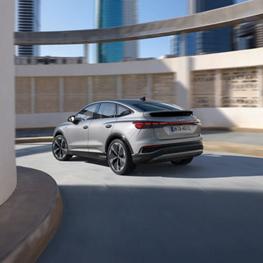 Rear view of silver Audi Q4 turning corner moving downhill.