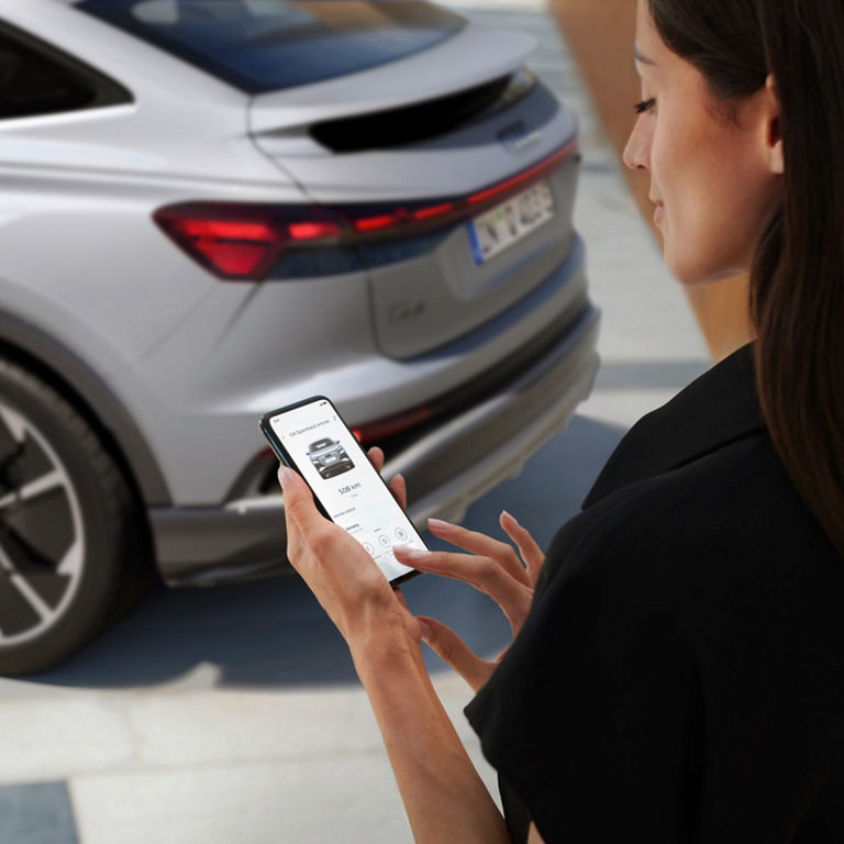 Lady using Audi phone app near Audi Q4 Sportback e-tron car.