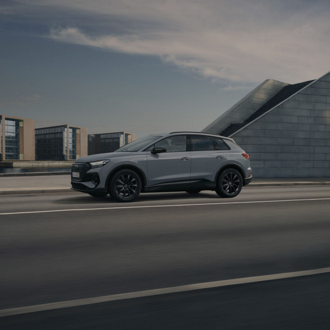 A modern SUV driving on a city road with buildings and a clear sky in the background.