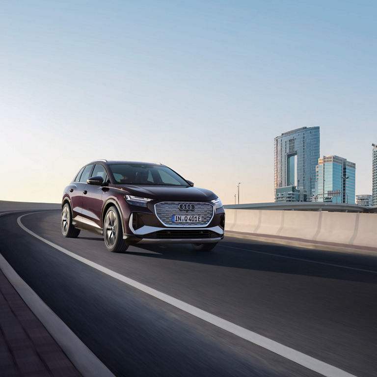 Audi Q4 e-tron travelling down a bridge road with city skyline in the background.