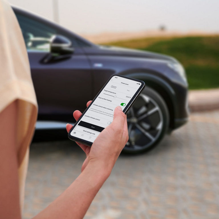 Person using a smartphone app to control car settings with a vehicle in the background.