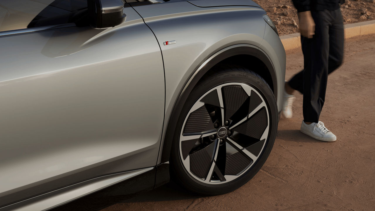 Close-up of a silver car's wheel and a person walking away.