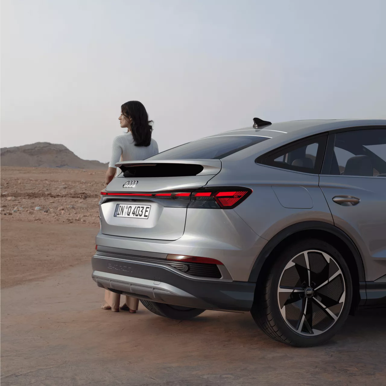 A person standing next to a silver car in a desert environment.