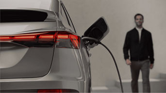 Electric car plugged into a charging station; a person stands nearby.