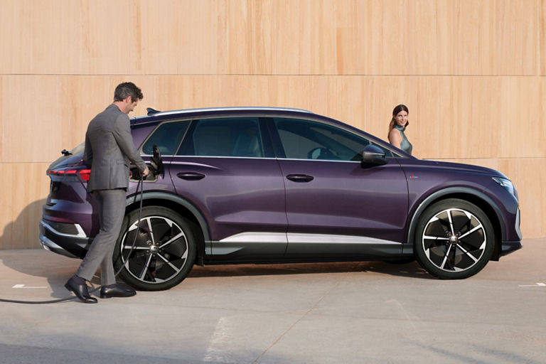 A person charging a purple electric SUV parked beside a wooden wall.