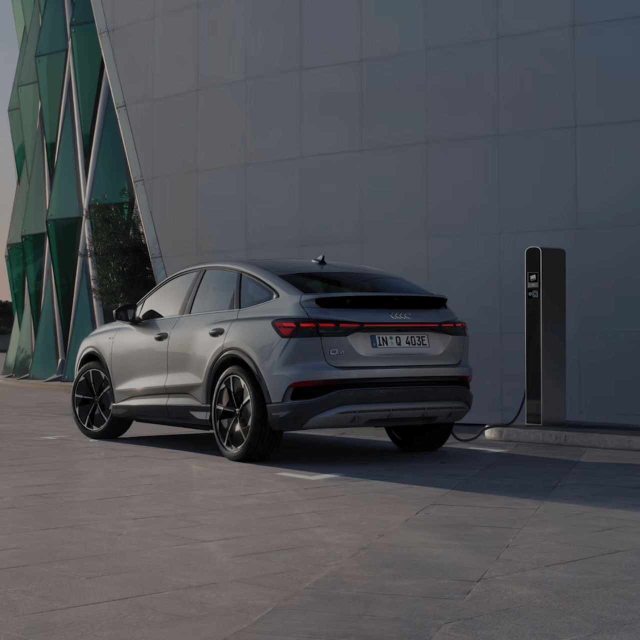 Silver electric car charging at a modern station against a geometric building facade.