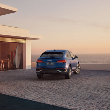A blue Audi parked on a coastal residence driveway at sunset.