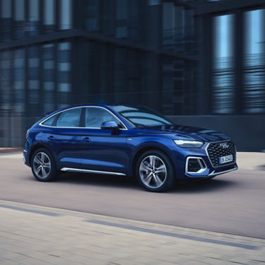 Blue car on the road with modern buildings in the background.