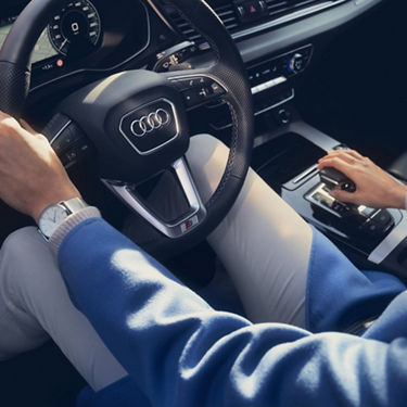 Driver's hands on an Audi steering wheel and gear shift, with focus on luxury interior.