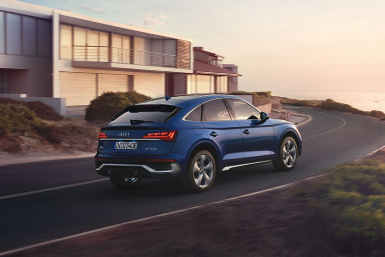 Blue SUV driving on coastal road at sunset.