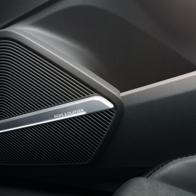 Car door speaker grille with "BANG & OLUFSEN" inscription, textured black interior.