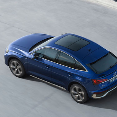 A blue Audi driving on an asphalt road, viewed from above.