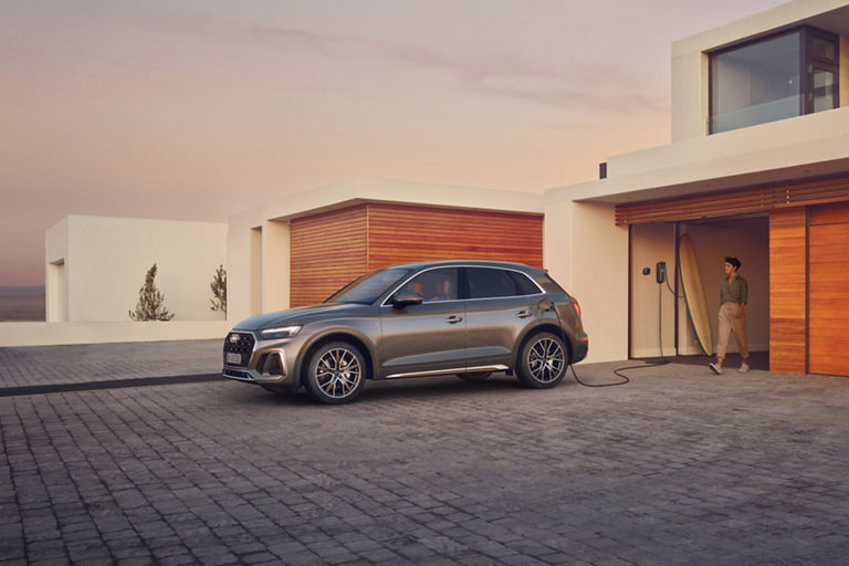 SUV charging at a modern home driveway during sunset.