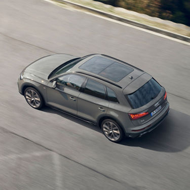 A grey car driving on a road, viewed from above.