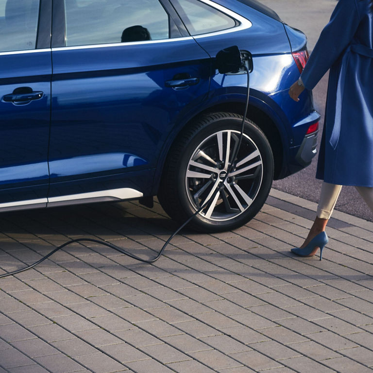 Person walking towards a blue electric car plugged into a charging station.