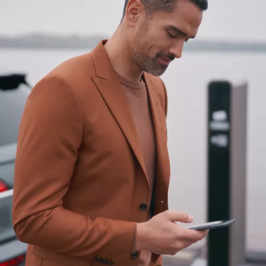 A person in a brown jacket holding a smartphone.