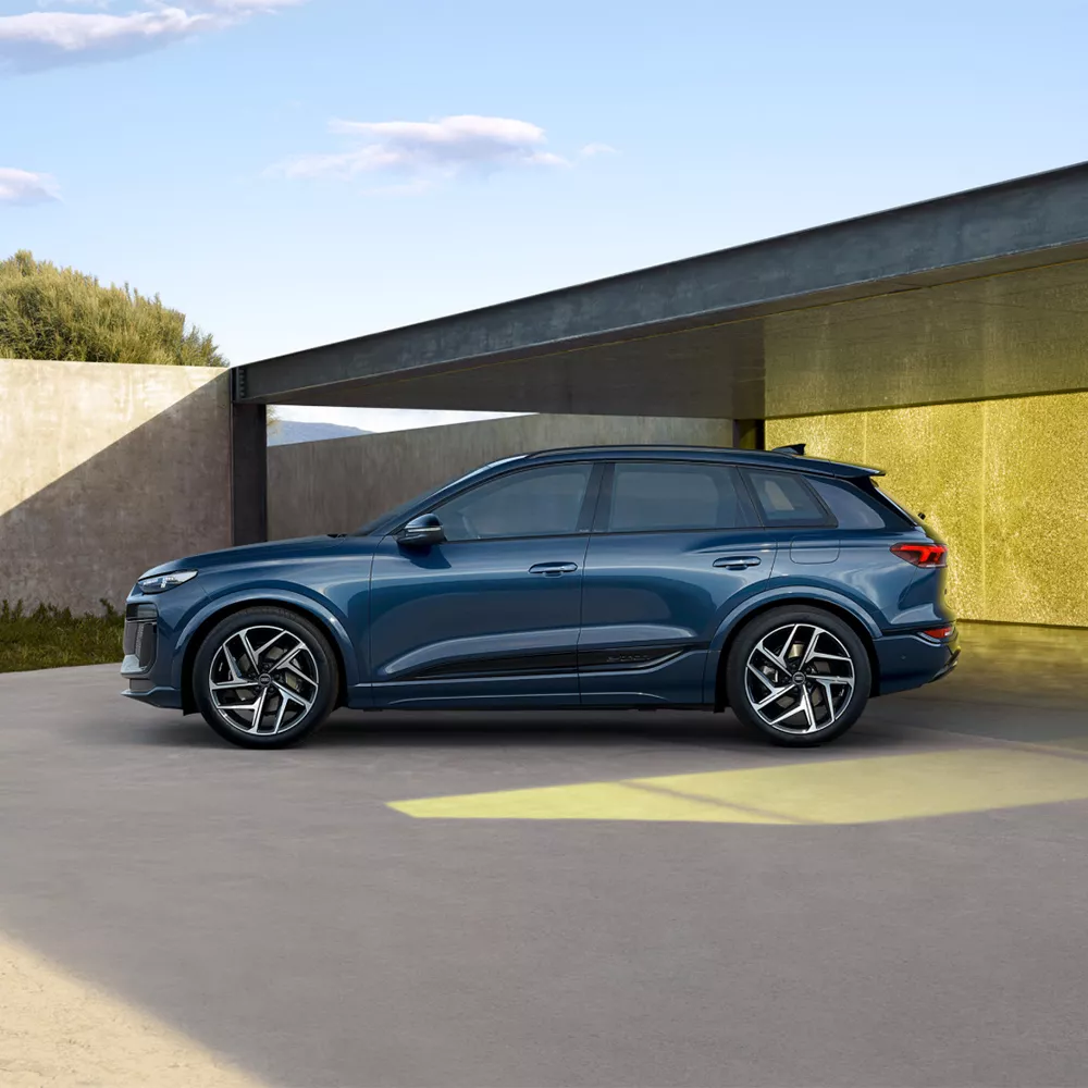 A blue SUV parked beside a concrete wall with gold paneling under sunlight.