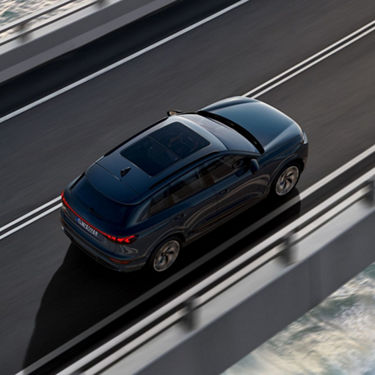 Aerial view of a blue car driving on a bridge over water.
