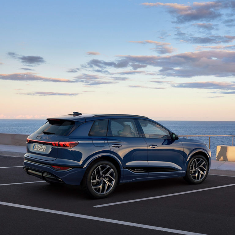 A blue SUV parked by the seaside at dusk, with a person walking in the background.