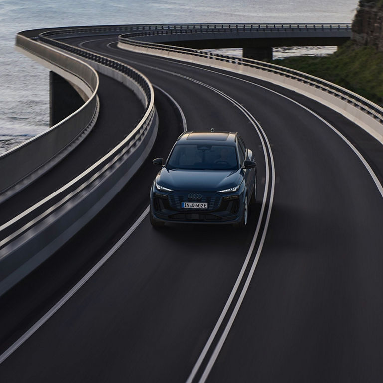 An Audi car driving on a curved coastal road with guardrails, ocean and cliffs in the background.