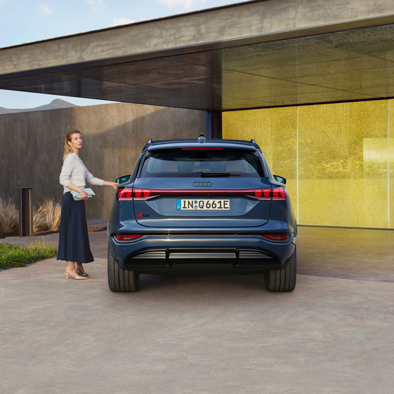 A woman walking towards a blue Audi e-tron parked in a modern driveway.