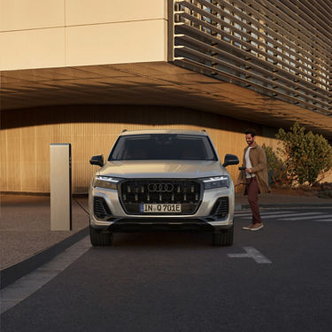 An Audi SUV parked at a charging station with a person holding a charging cable.