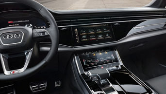 Interior of a car with dual touchscreens on the dashboard and a leather steering wheel.