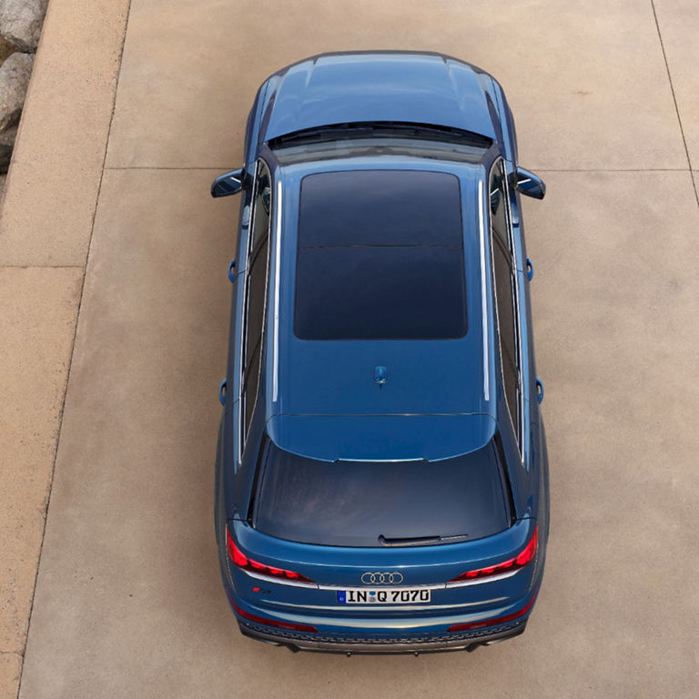 A blue sedan parked on a pier by the sea, viewed from above.